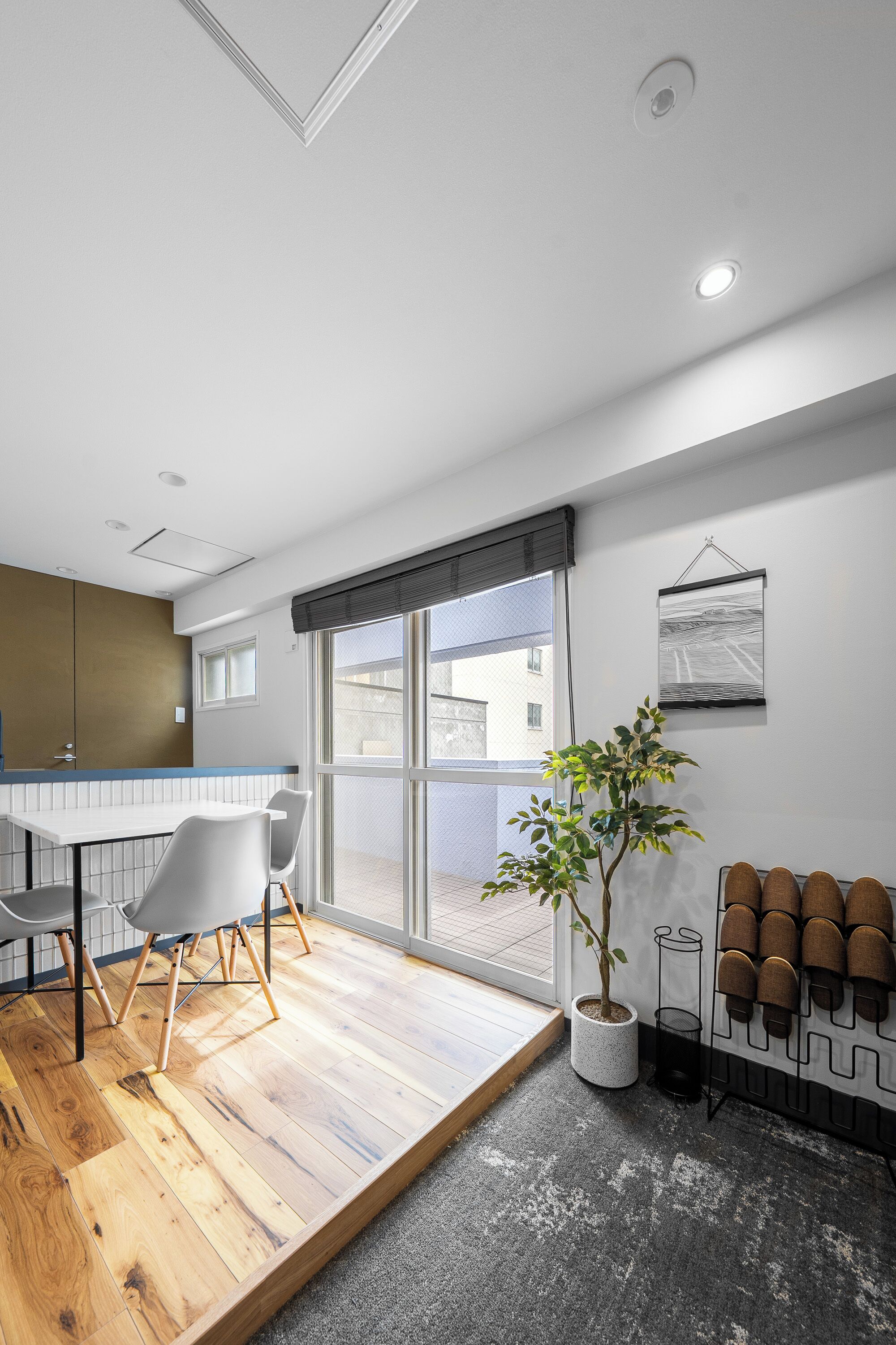 Une cuisine moderne avec un plancher en bois, un coin repas avec des chaises, une plante en pot et un porte-chaussures fixé au mur.