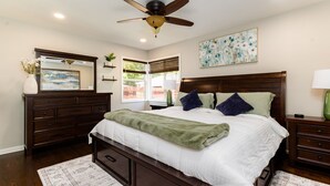 A bedroom with a large bed, wooden headboard, a ceiling fan, a painting, a mirror, a dresser, and a window with blinds. - The Dome Home<>3BR House 1mi to ND (South Bend)