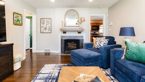 A living room with a fireplace, blue sofas, a coffee table, and a television. - The Dome Home<>3BR House 1mi to ND (South Bend)