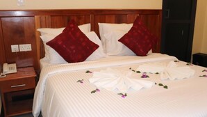 A neatly made bed with white linens and red pillows, a bedside telephone, and a wooden headboard. - Blue Junction Eco Lodge (Arusha)