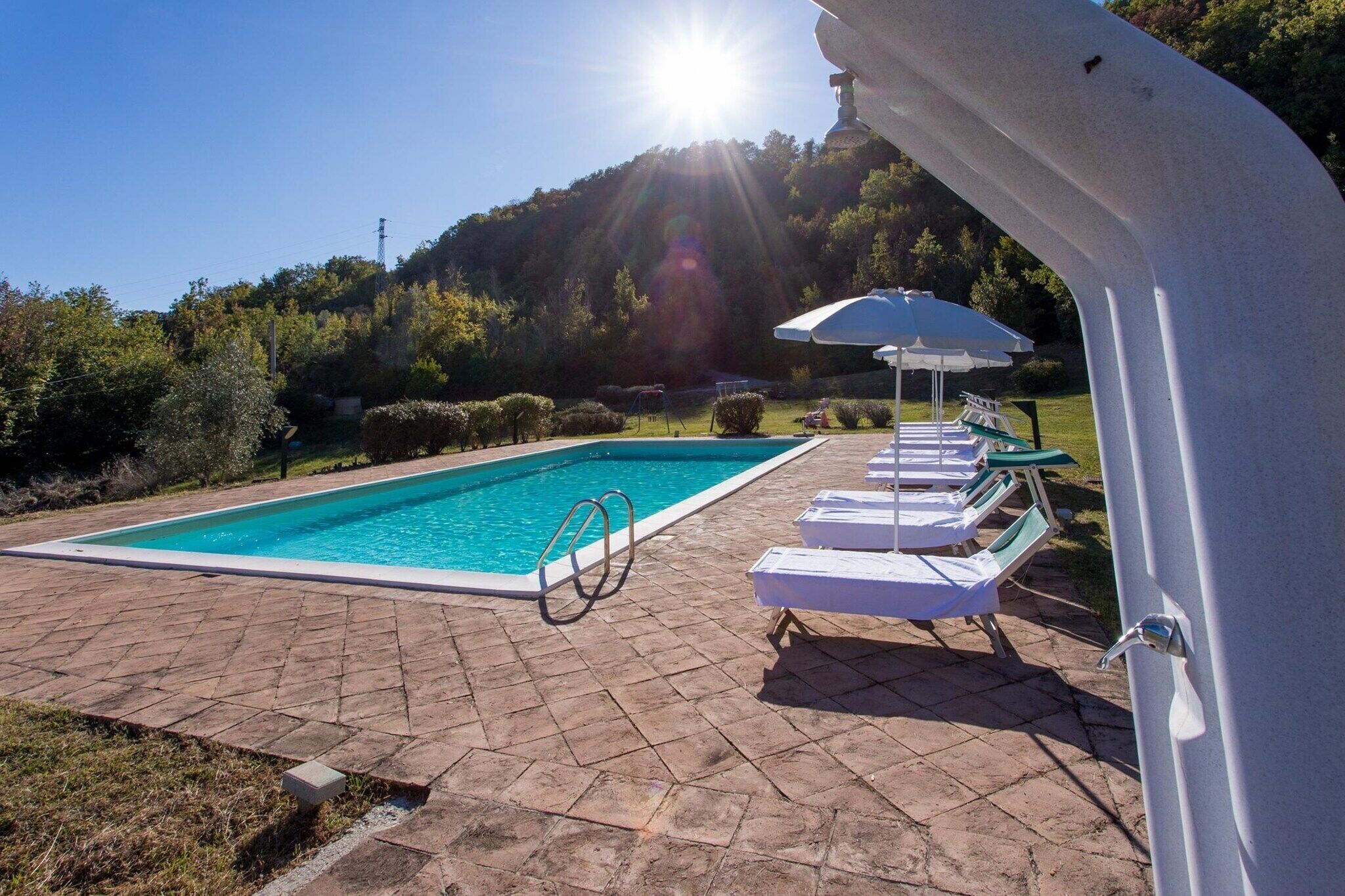 Una piscina con lettini e un ombrellone, circondata da un patio in mattoni e vegetazione.