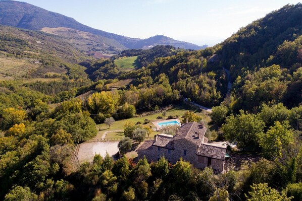 A stone house with a swimming pool surrounded by lush greenery and hills.