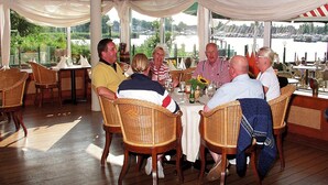 Un groupe de personnes est assis à une table, avec une vue sur une étendue d’eau et des bateaux en arrière-plan.