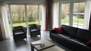 Un salon moderne avec un canapé en cuir noir, deux fauteuils en osier et une table basse.