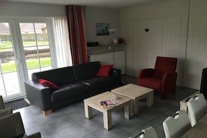 Una sala de estar moderna con un sofá negro, un sillón rojo y una mesa de centro de madera.