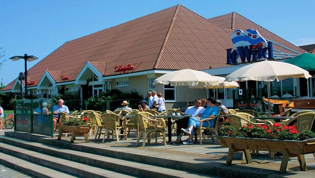 Un espace extérieur aménagé avec des chaises et des tables en osier, un bâtiment doté d’un toit rouge et une enseigne sur laquelle on peut lire « Hewlett ».