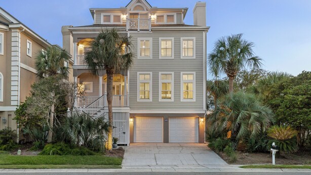 A two-story house with a front porch, a garage, and a well-maintained garden with palm trees.