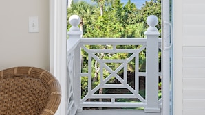 A balcony with a white railing, a wicker chair, and a view of greenery and the ocean.