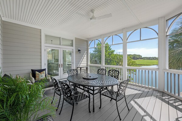 A covered patio with a round table and chairs, large windows, and a view of a green landscape.