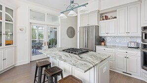 A modern kitchen with white cabinetry, a marble island, and stainless steel appliances.