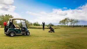 A golf course with a golf cart, a stroller, and people.