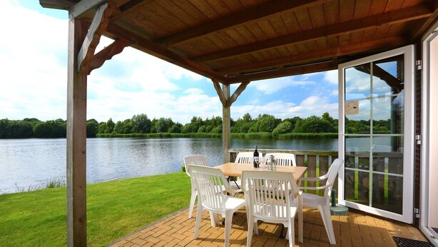 A covered patio with a table and chairs overlooking a lake.