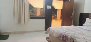 A bedroom with a bed, a window, and a door leading to a balcony. - Mridul Homestay Orchha  (Orchha)