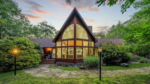 A cozy lodge with a large glass front, stone pathway, and lush greenery.