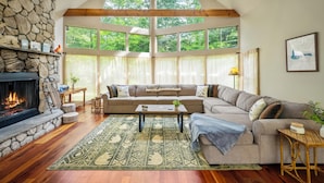 A cozy living room with a stone fireplace, a large window, a sectional sofa, and a coffee table.