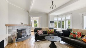 A living room with a fireplace, black leather sofa, and a round coffee table. - Talina - History in the Heart of St Helens (Break O'Day)