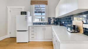 A modern kitchen with white cabinets, a built-in microwave, a toaster, and a window with a view. - Talina - History in the Heart of St Helens (Break O'Day)