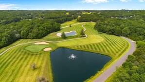 Vista aérea de un campo de golf con un estanque, búnkeres de arena y un camino sinuoso.