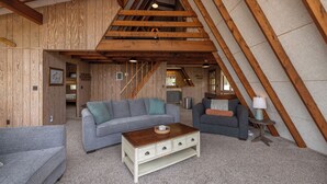 Un salón estilo loft con vigas de madera a la vista, un sofá gris, una mesa de centro de madera y una mesita auxiliar con una lámpara.