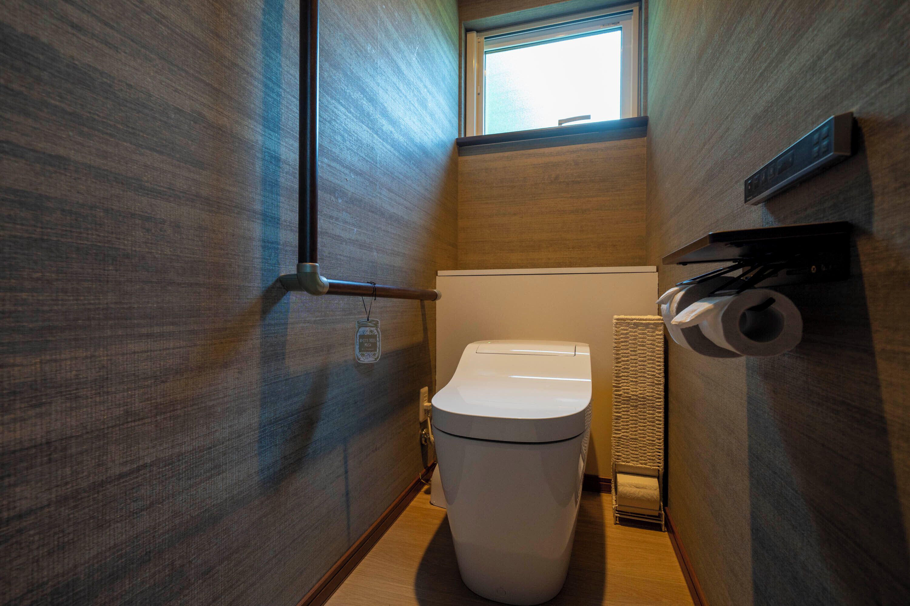 A compact bathroom with a toilet, a towel rack, and a window.