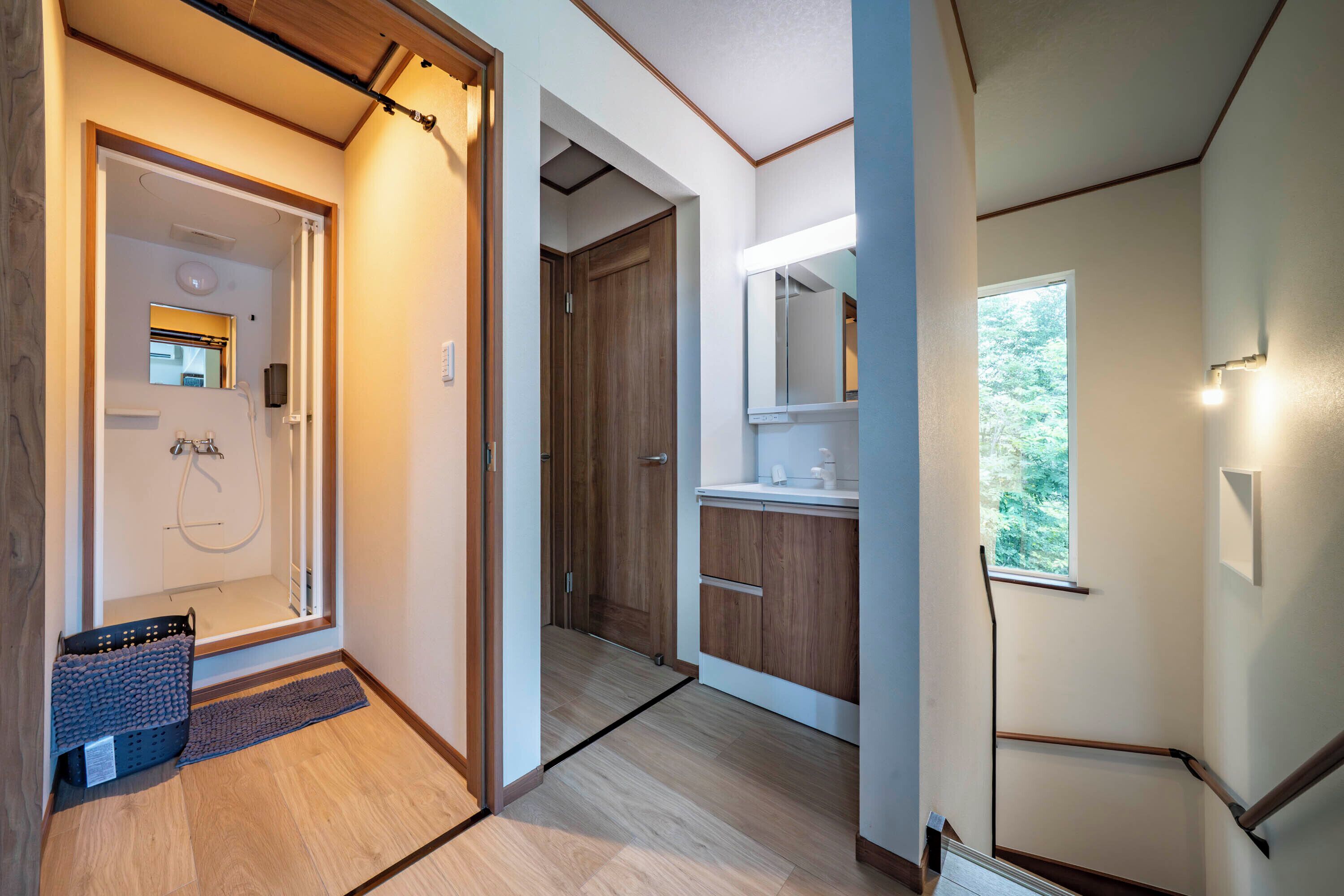 A hallway with wooden flooring, a shower area, and a window providing natural light.