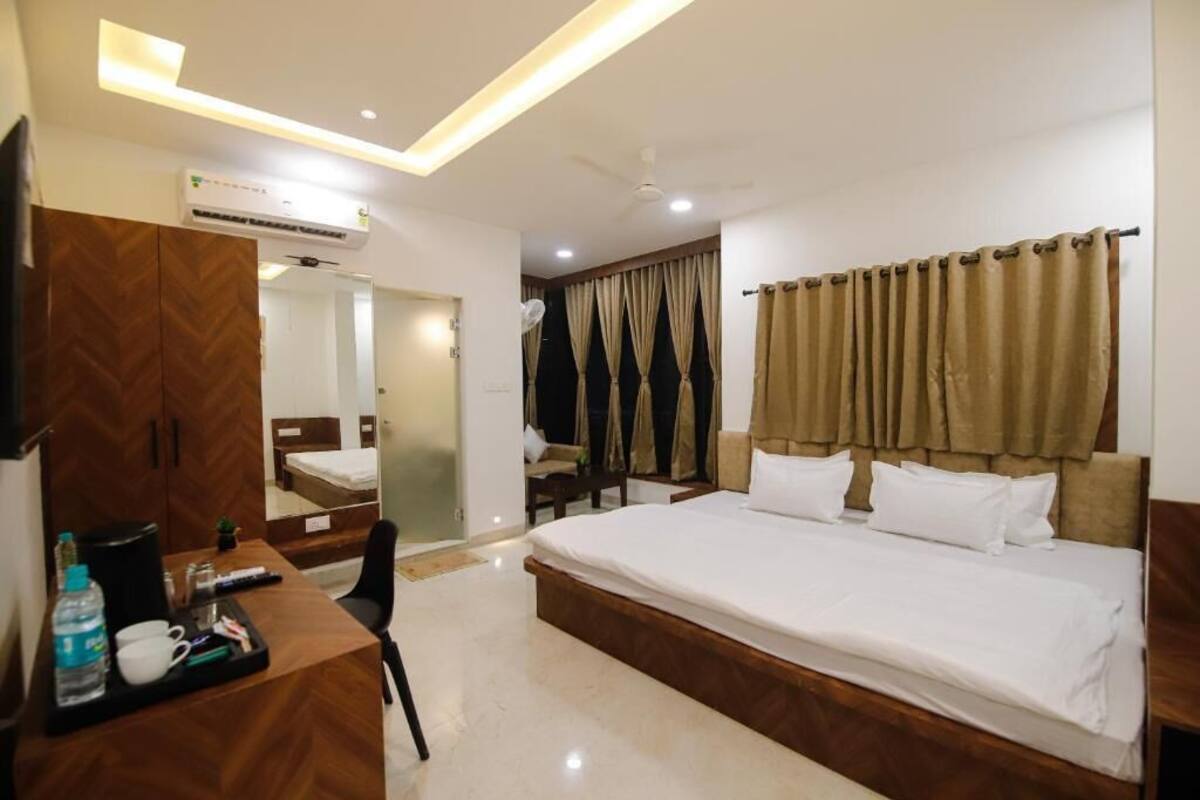A hotel room with a bed, a desk with a chair, a wardrobe, an air conditioning unit, and a ceiling fan.