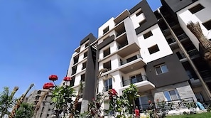A multi-story residential building with balconies, a clear sky, and some greenery.