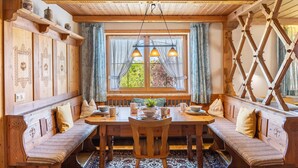 Ein Essbereich mit Holzbänken, einem Tisch gedeckt mit Tellern und Tassen sowie einem Fenster mit Vorhängen.