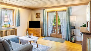 Ein gemütliches Zimmer mit Holzboden, einem Fernseher, einem Sofa, einem Tisch mit einem Glas und einem Schrank.