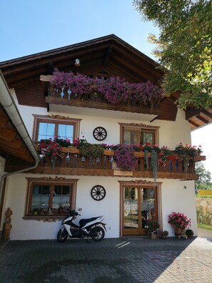 A two-story building with a balcony adorned with flowers, a motorcycle parked in front, and a sign indicating a nearby location.