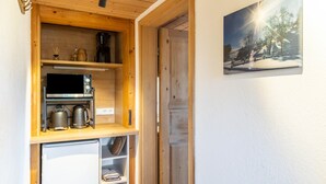 Et kompakt køkken med en Bosch mikrobølgeovn, kaffemaskine og elkedel, træskabe og et lille køleskab.
