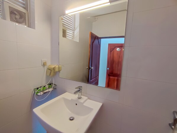 Une salle de bain avec un lavabo blanc, un miroir et un sèche-cheveux fixé au mur.