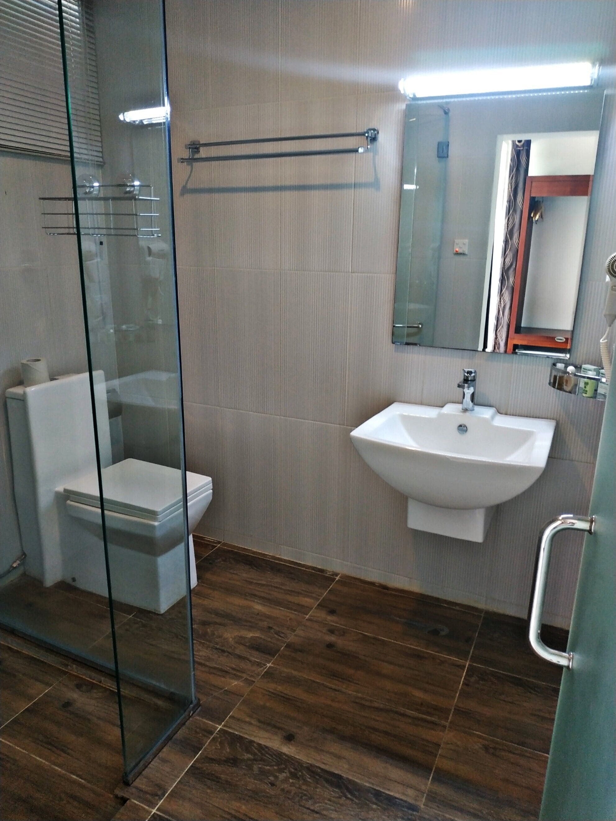 Un baño moderno con cabina de ducha de vidrio, un inodoro blanco, un lavabo con espejo y suelo de madera.