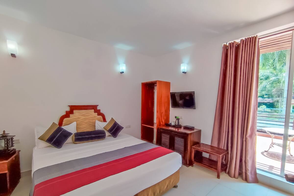 A hotel room with a bed, a TV, a desk, and a window with curtains.