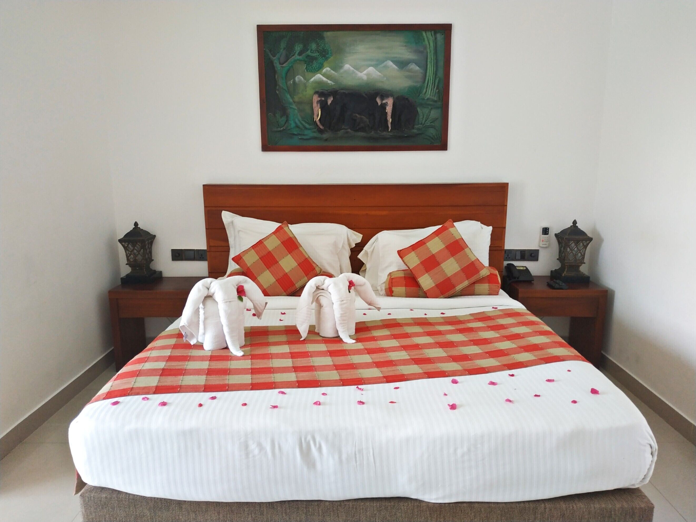 Una cama bien hecha con una colcha a cuadros, dos almohadas y una manta. Hay dos mesitas de noche con lámparas y un cuadro sobre la cama.