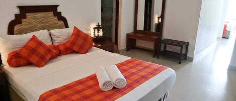 Una cama bien hecha con una manta escocesa, dos almohadas y toallas enrolladas. Junto a la cama hay una mesita de noche de madera con un farol. Un banco de madera y un espejo están apoyados en la pared.