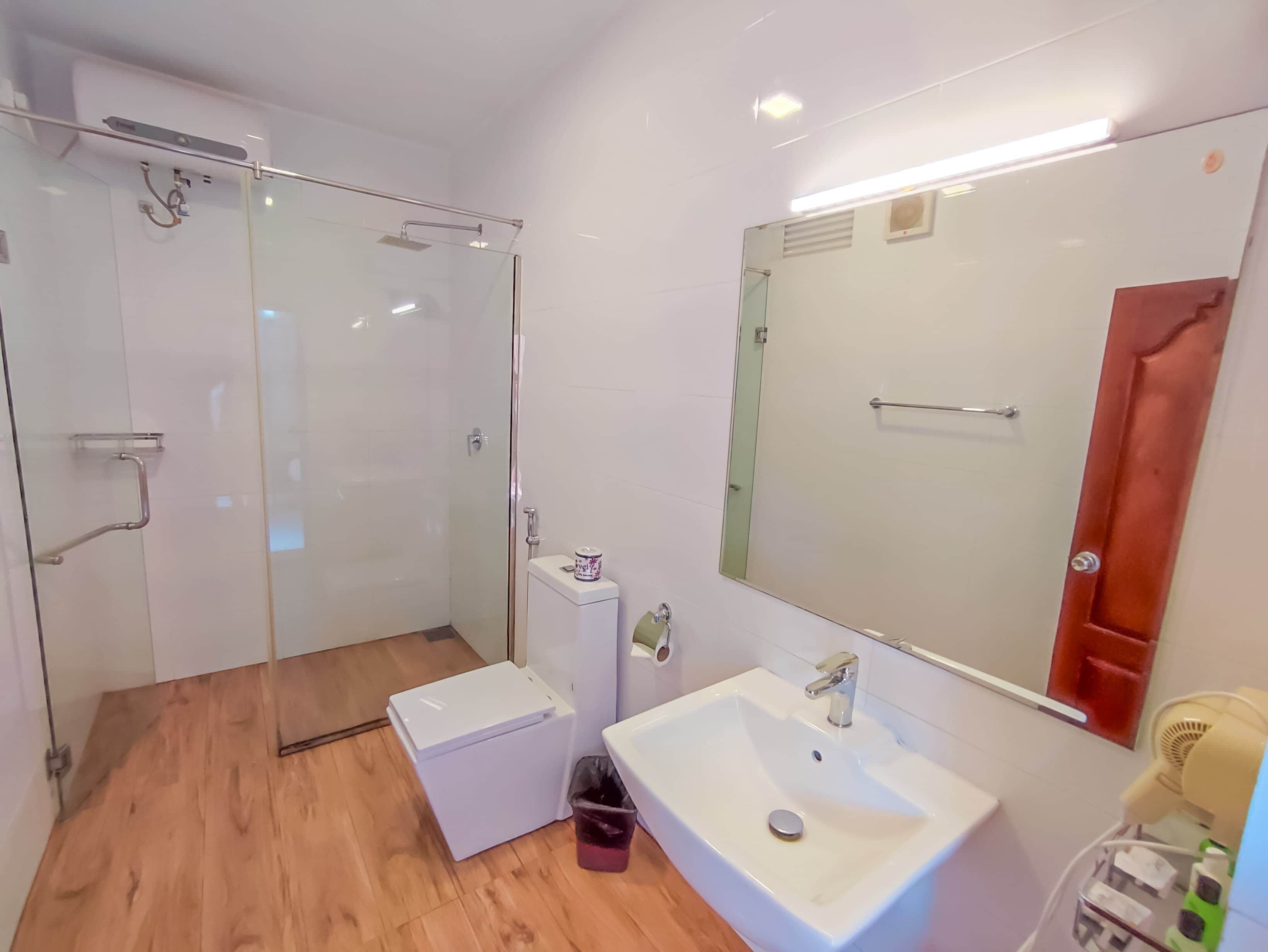 A modern bathroom with a glass shower enclosure, a white sink, and a small trash bin.