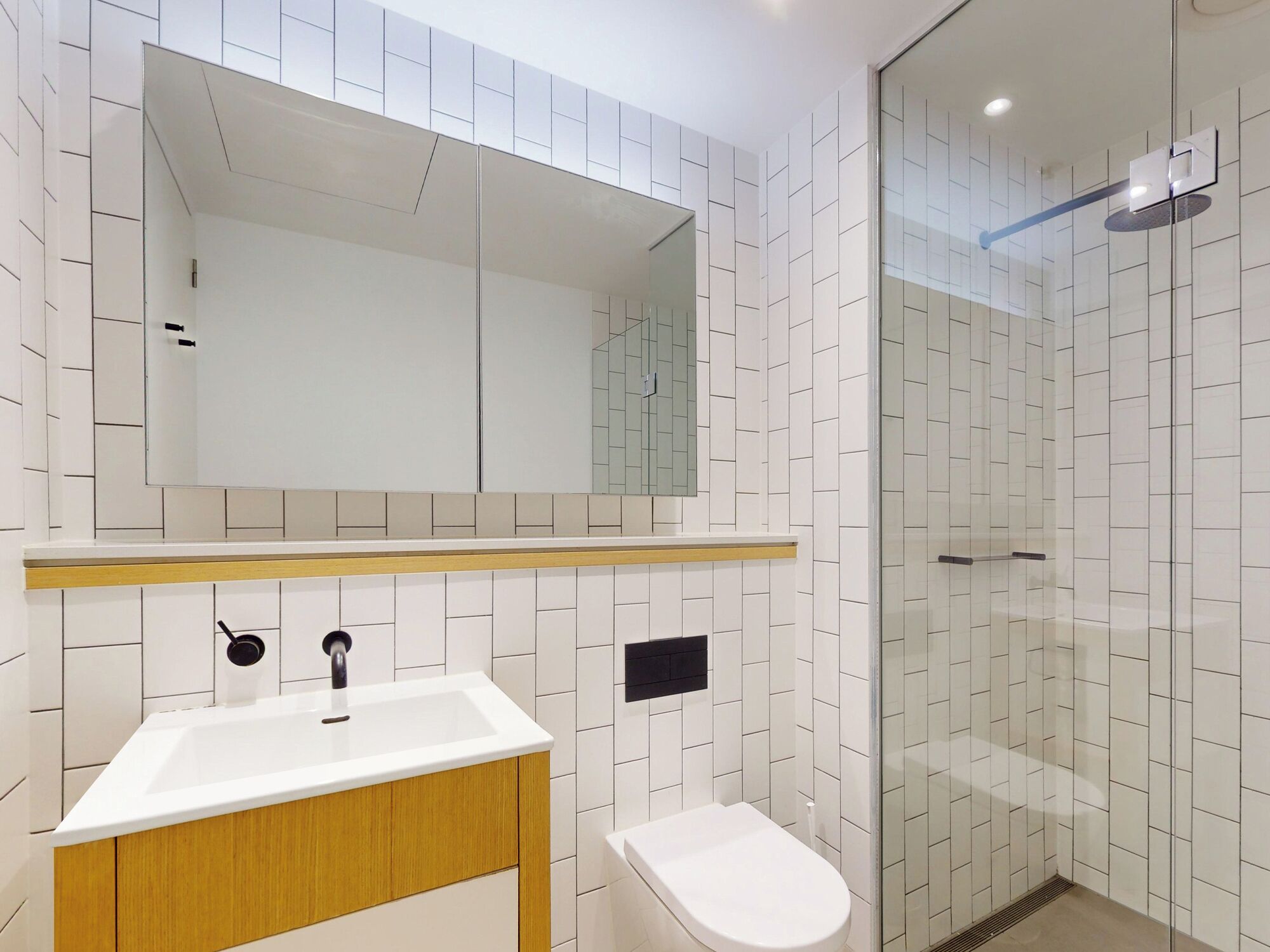 A modern bathroom with a white sink, wooden vanity, a mirror, and a glass shower enclosure.