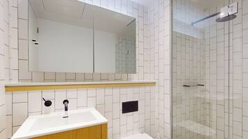 A modern bathroom with a white sink, wooden vanity, a mirror, and a glass shower enclosure.
