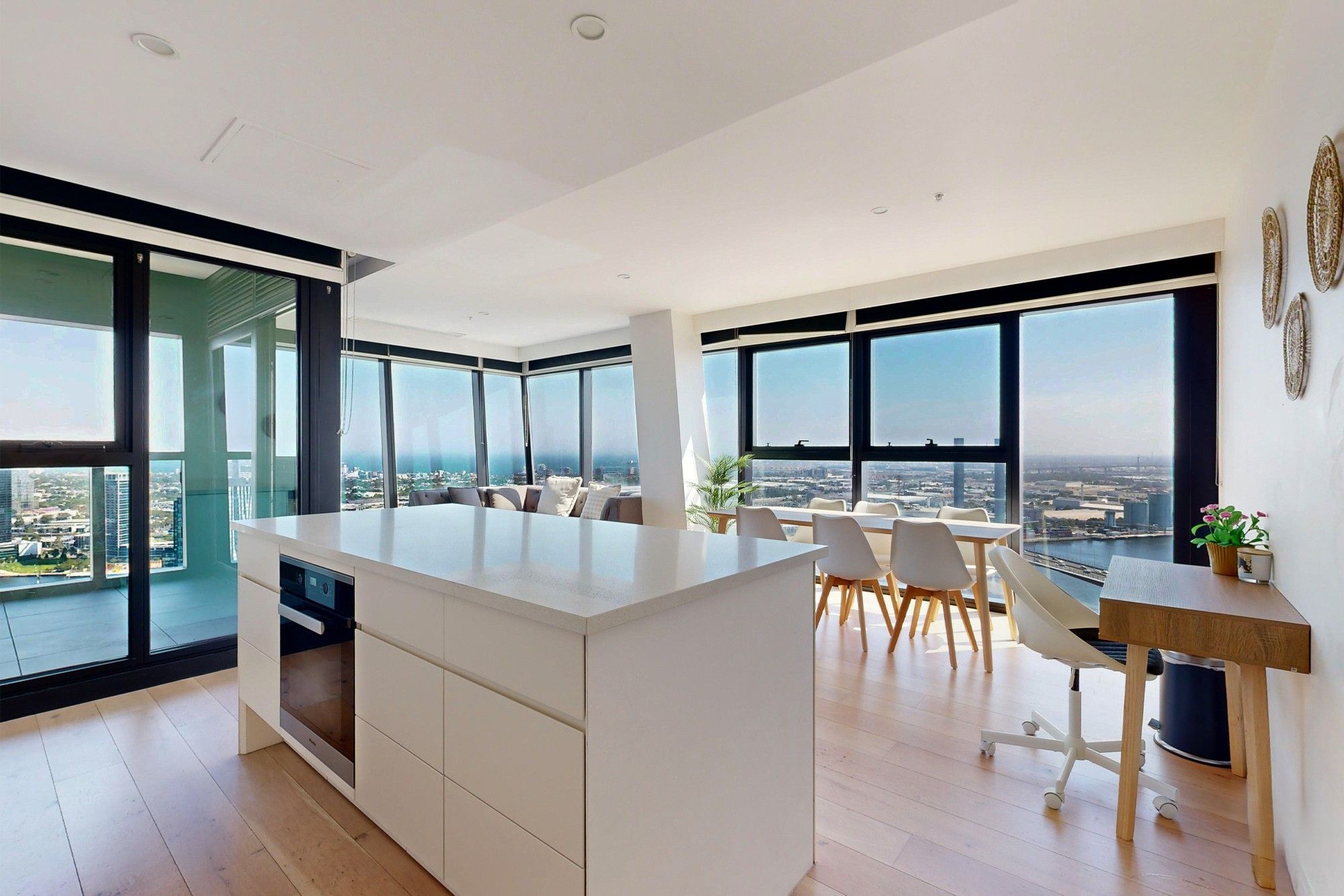 A modern office space with a large island desk, white furniture, and large windows offering city views.