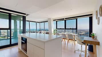 A modern office space with a large island desk, white furniture, and large windows offering city views.