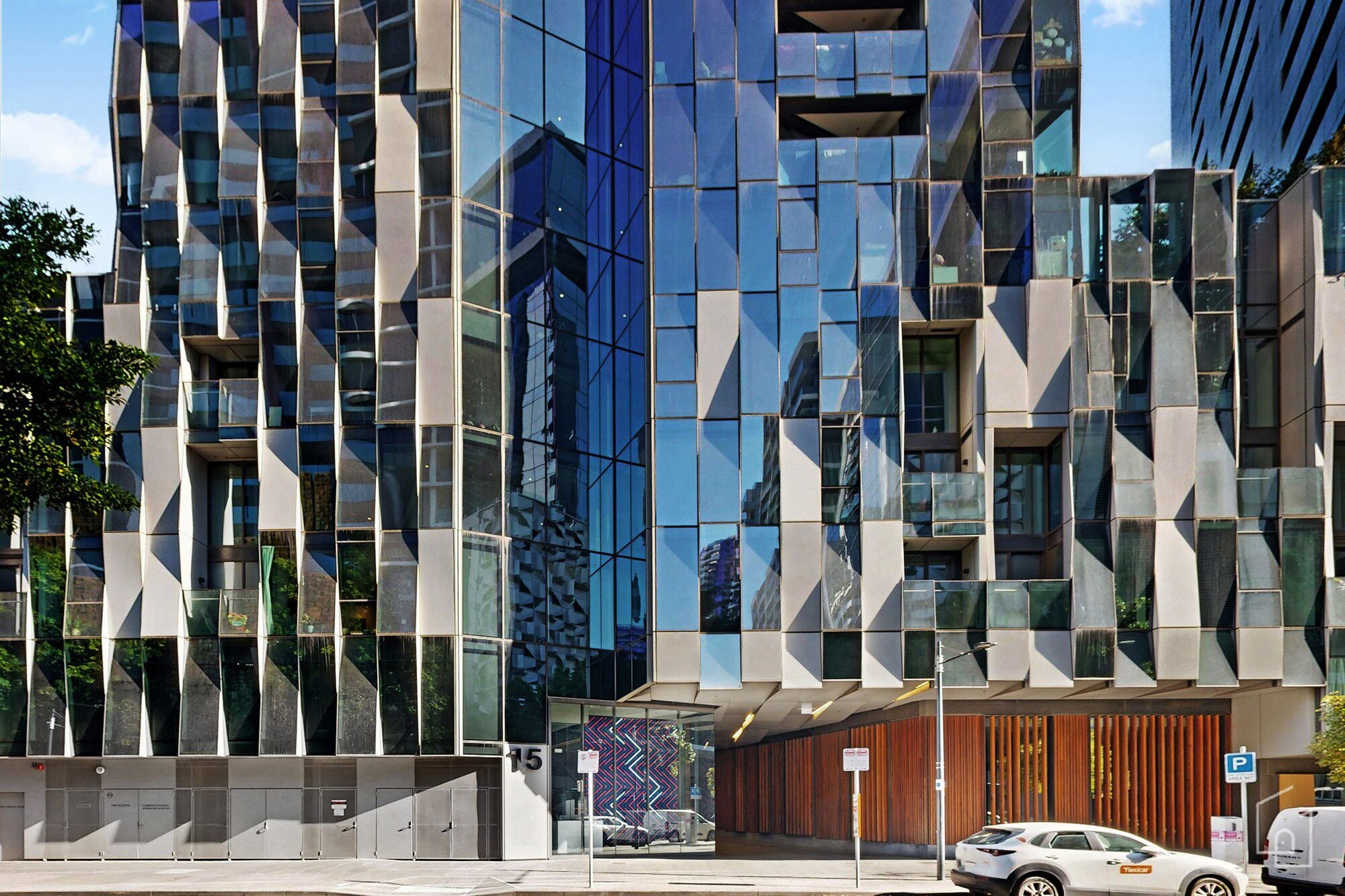 A modern building with a geometric facade, large windows, and a visible entrance with a car parked outside.