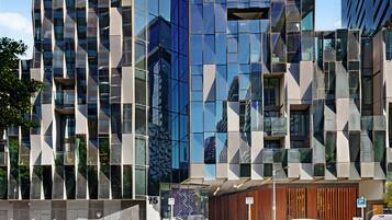 A modern building with a geometric facade, large windows, and a visible entrance with a car parked outside.