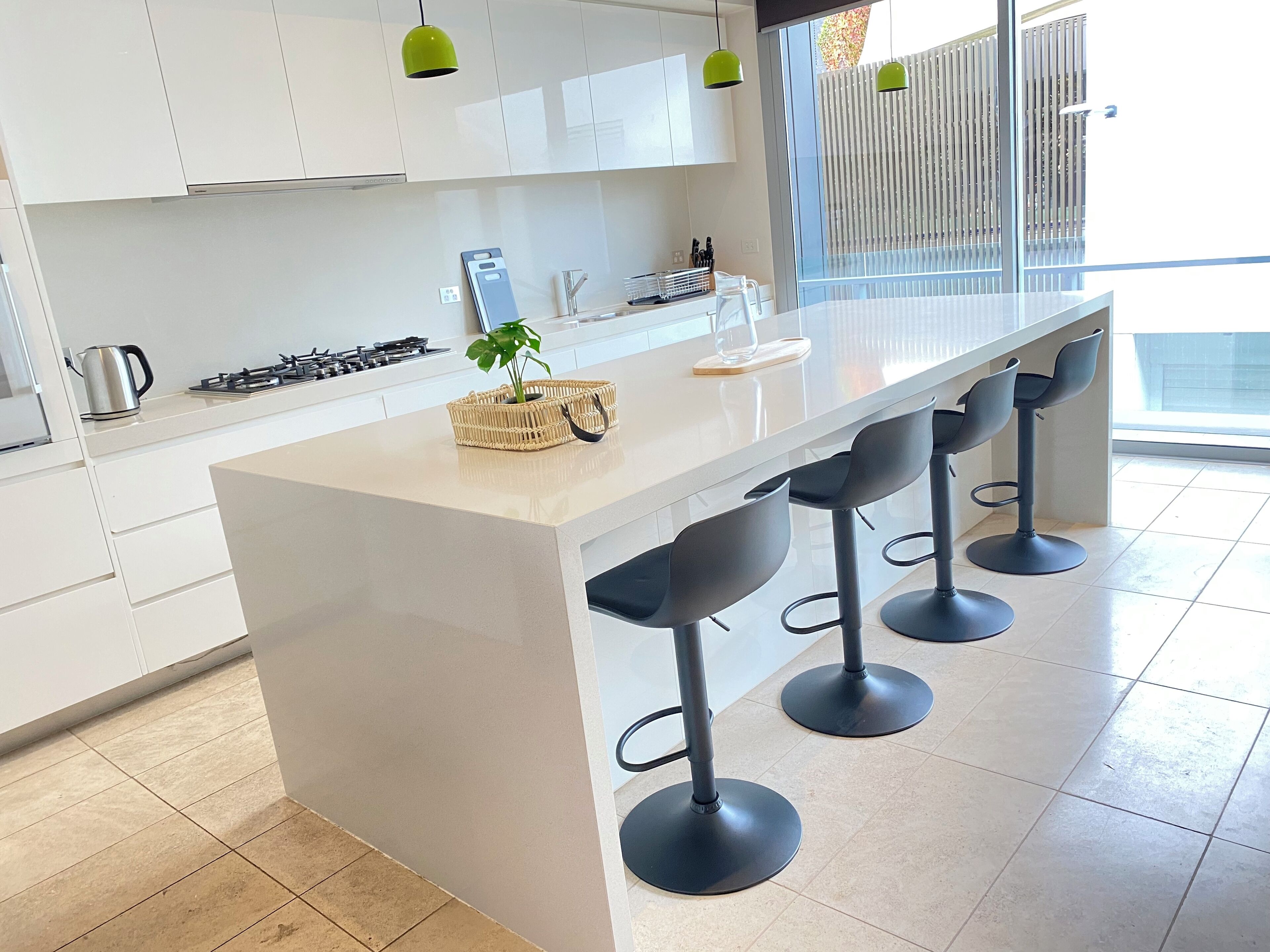 A modern kitchen with white cabinets, a central island with bar stools, a gas stove, and a hanging green pendant light.