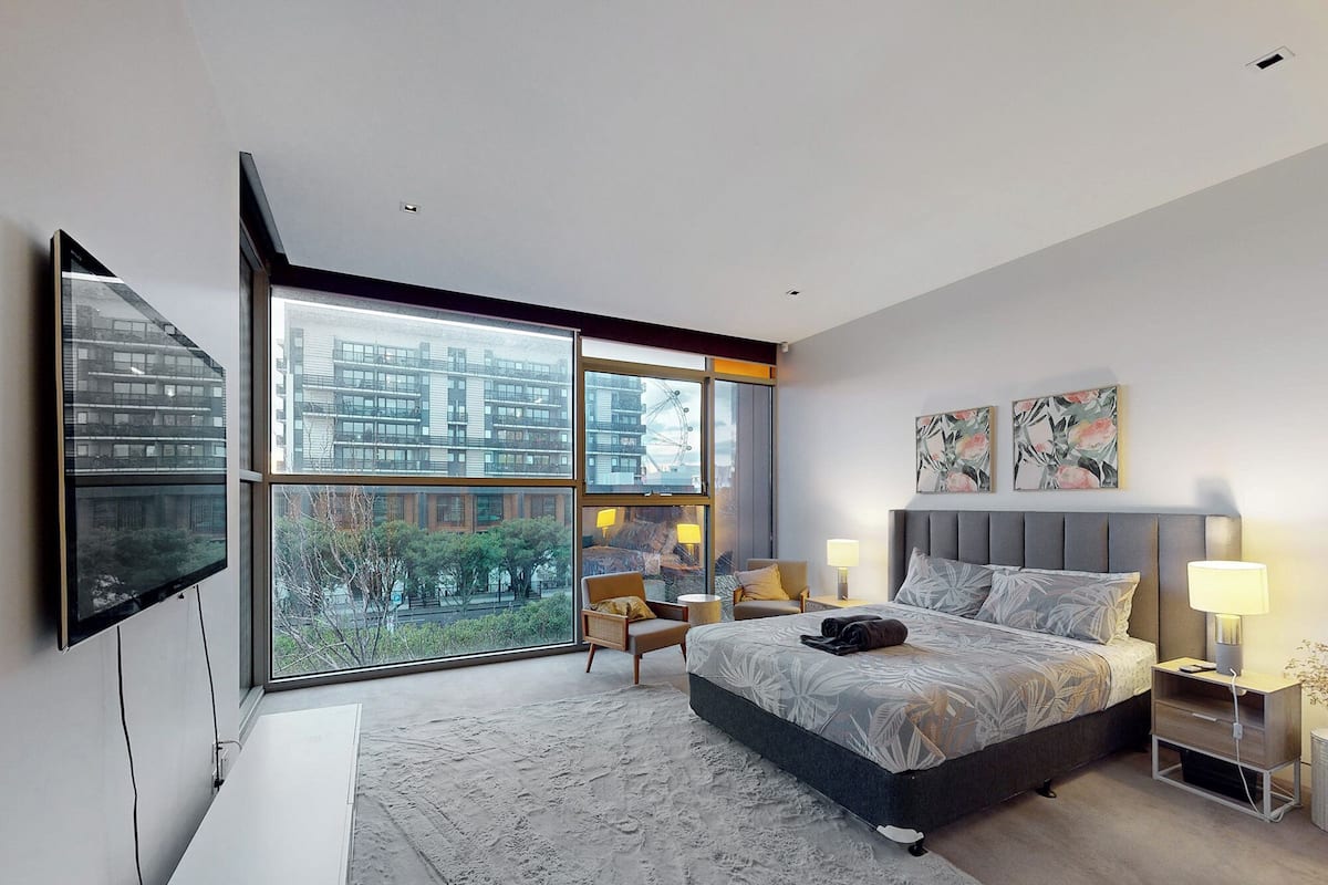 A modern bedroom with a large window, a bed, a chair, and a TV.