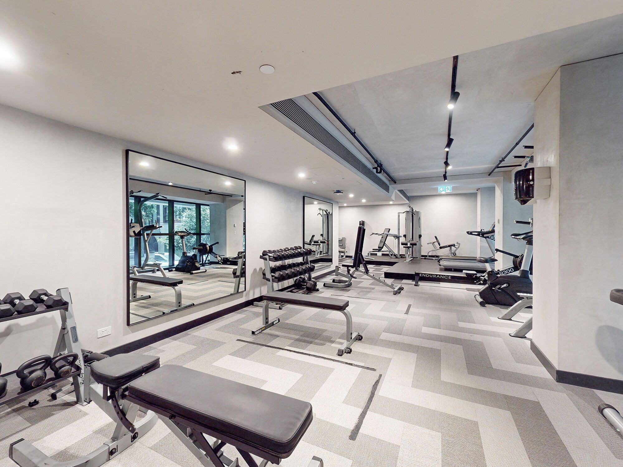 A modern gym with various exercise equipment, a bench, and a mirrored wall.