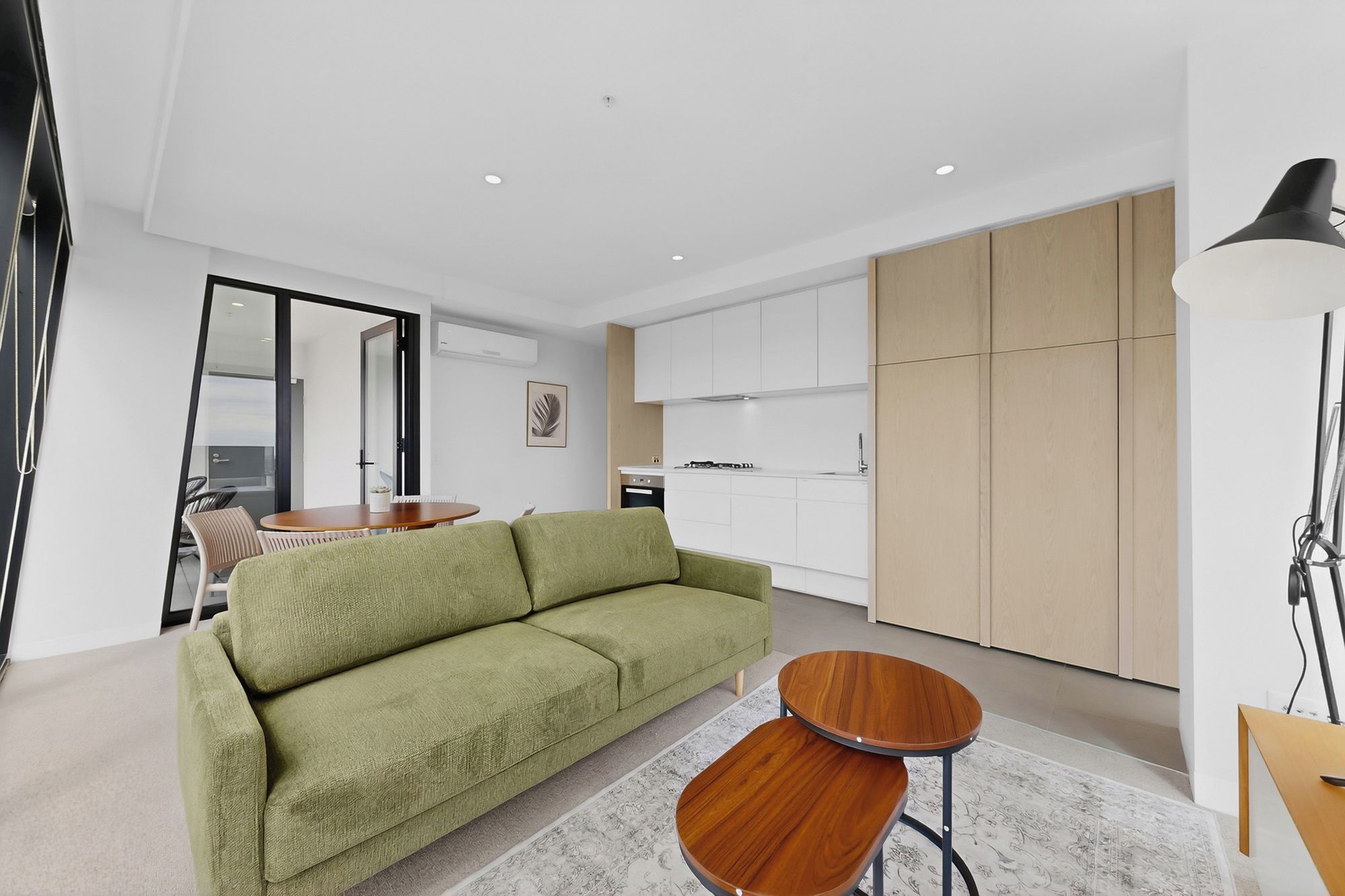 A modern living room with a green sofa, a wooden coffee table, and a dining area with chairs.