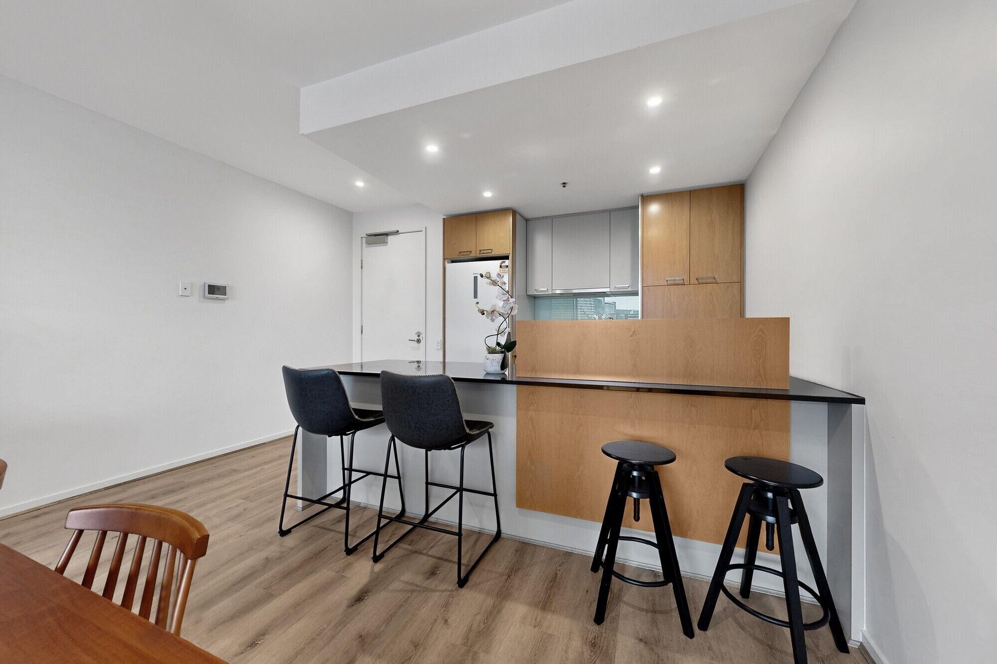 A modern kitchen with a central island, bar stools, and a dining area with a wooden table and chairs.