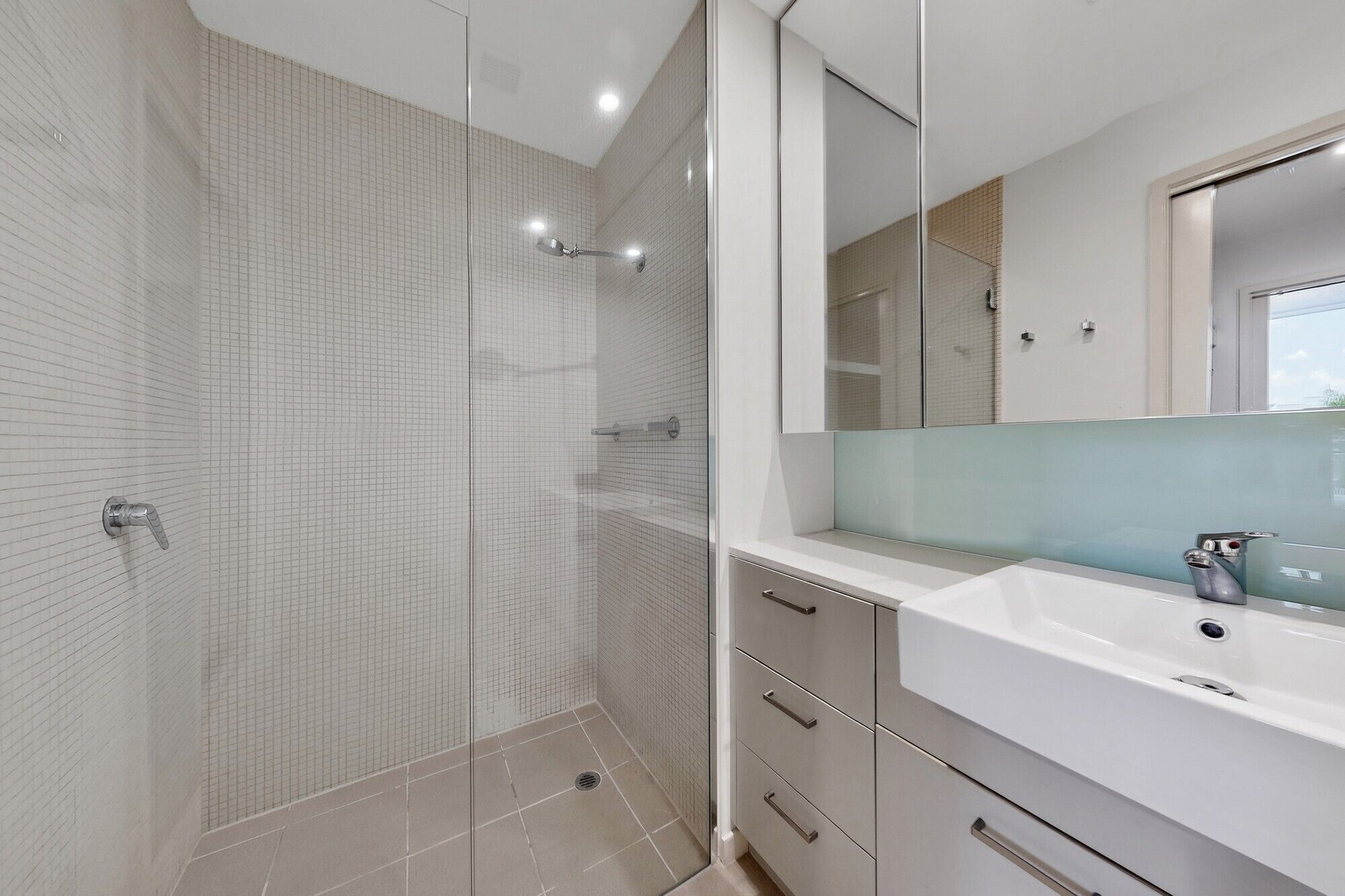 Un baño moderno con cabina de ducha de vidrio, un lavabo blanco y un espejo grande.