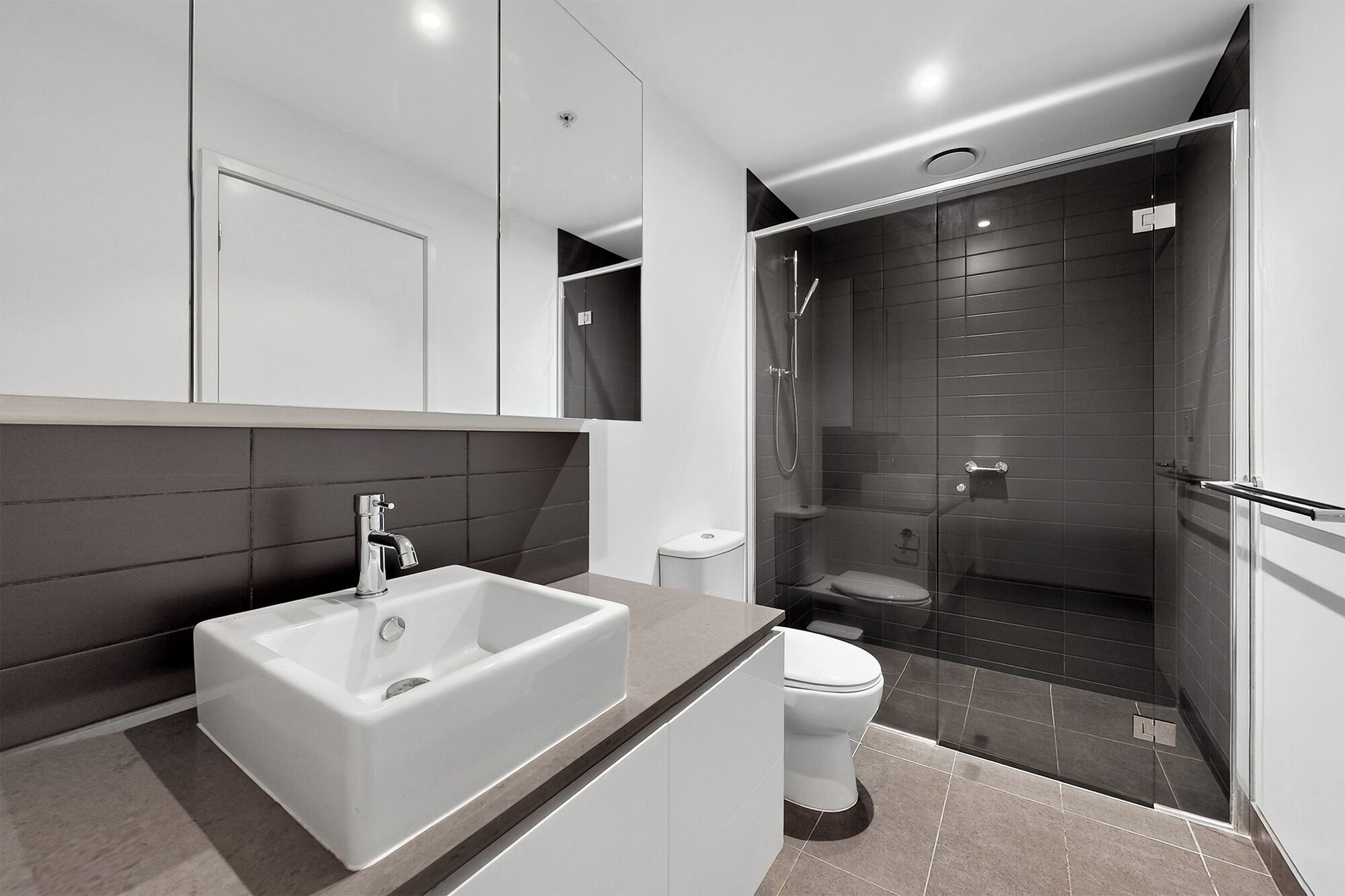 Une salle de bain moderne avec un grand lavabo blanc, des toilettes et une douche séparée par une paroi de verre.